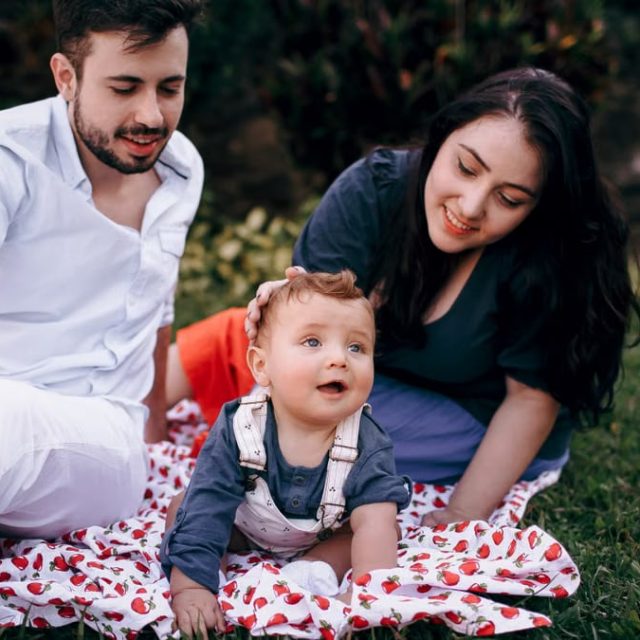 A joyful family enjoying a picnic outdoors during summer. Smiling parents with their baby on a blanket.
